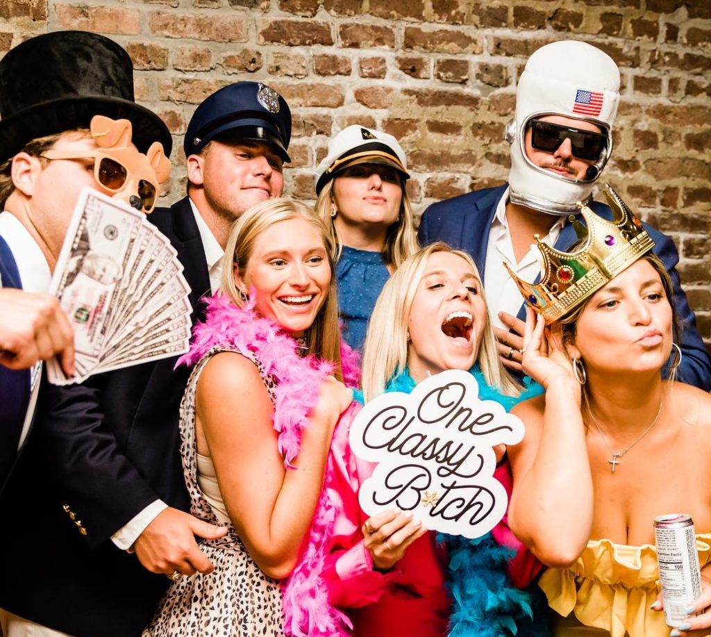 Group of guests posing with props, signs, and accessories in an ML Event Entertainment photobooth.